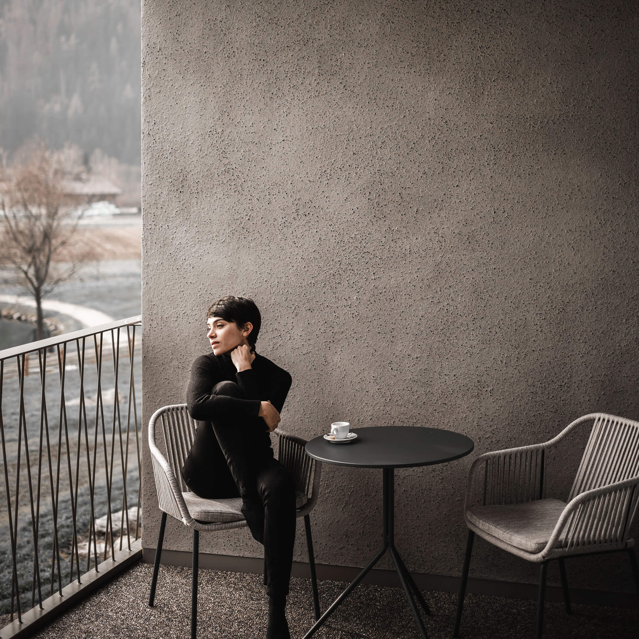 Frau sitzt mit einem Kaffee auf einem Stuhl auf dem Balkon und schaut in die Natur - OLM Nature Escape