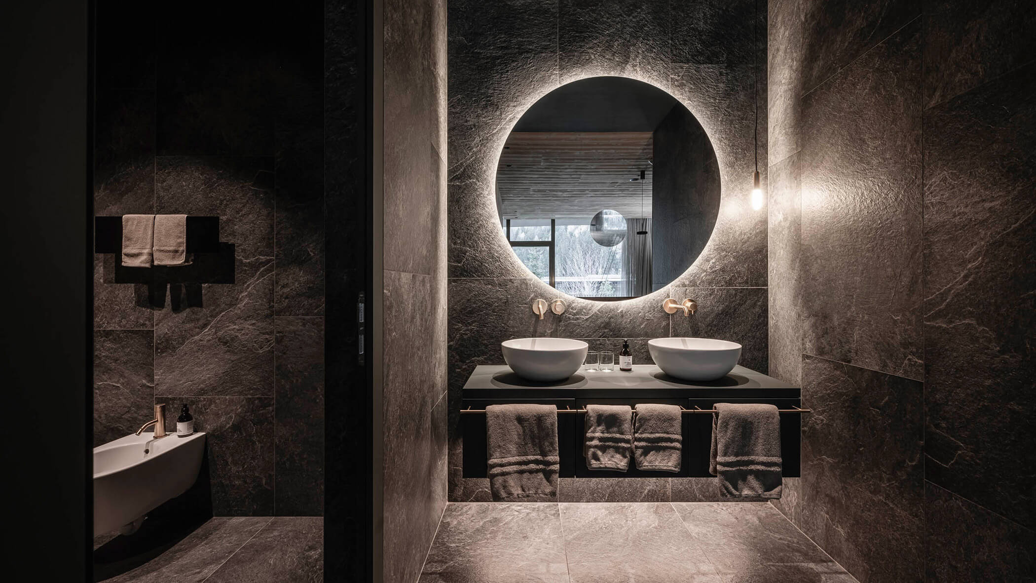 Indirekte Beleuchtung vom Waschbeckenspiegel in einem schwarz gefliestem Badezimmer - OLM Nature Escape