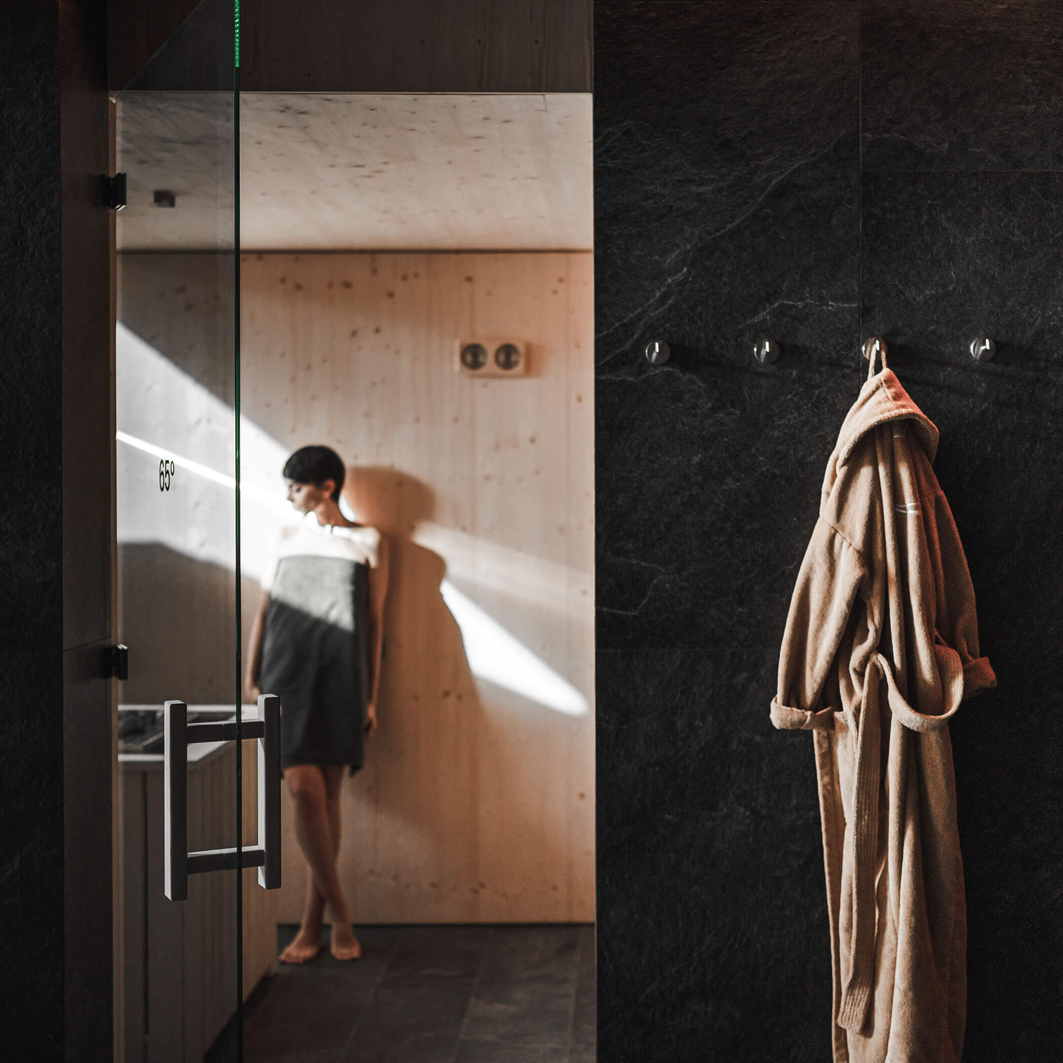 Frau steht in der Sauna - im Vordergrund hängt ihr Bademantel - OLM Nature Escape