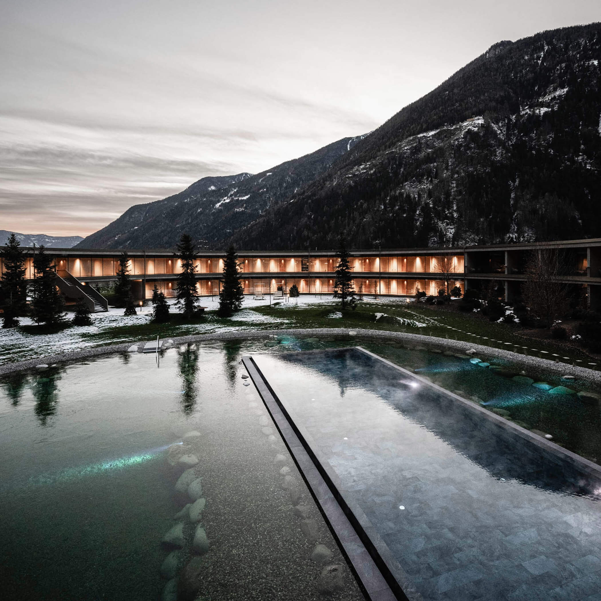 Outdoor pool and illuminated natural swimming pond in the evening - OLM Nature Escape